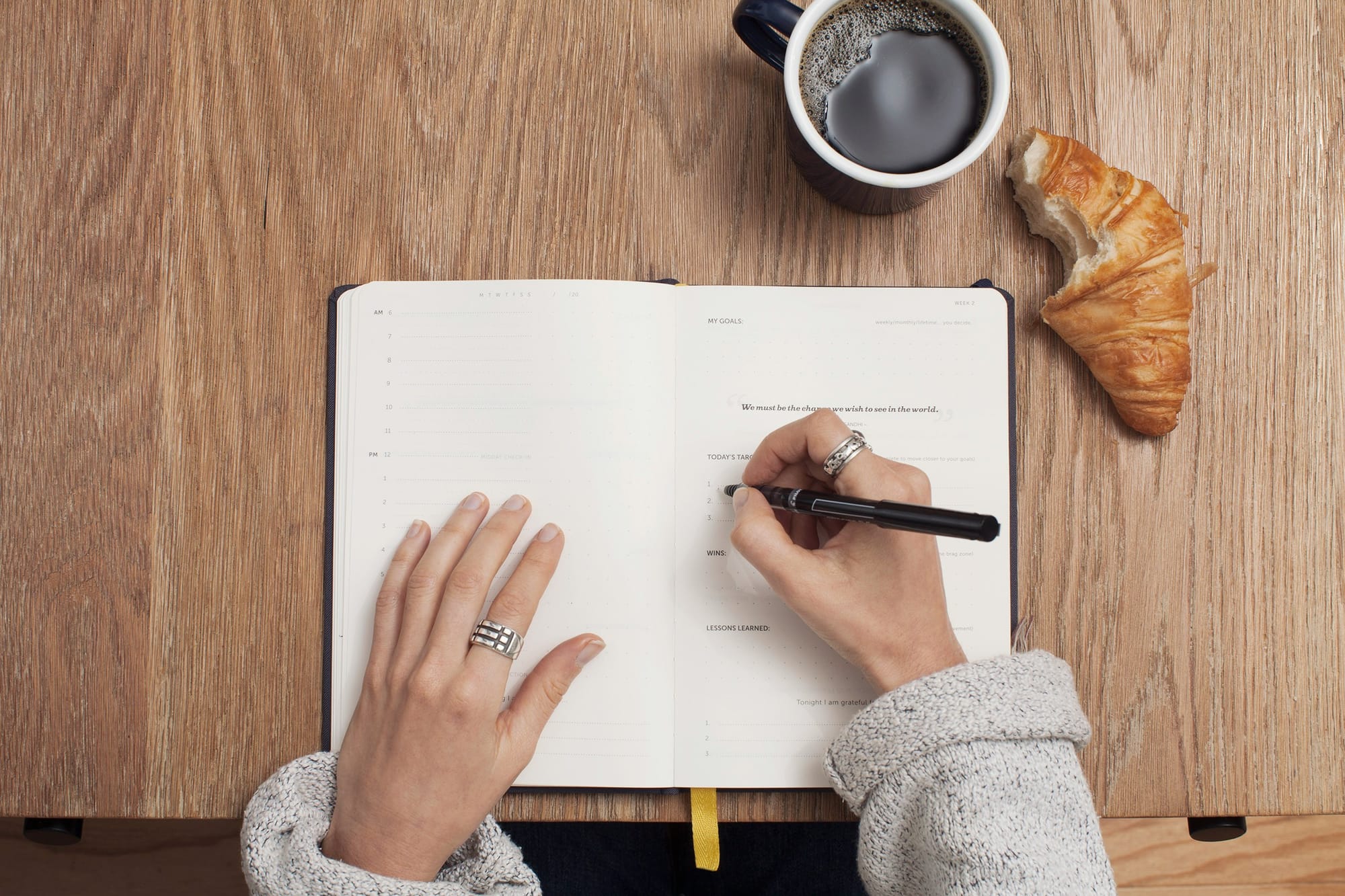 Woman's hands writing on a notebook with a coffee and a croissant on the table