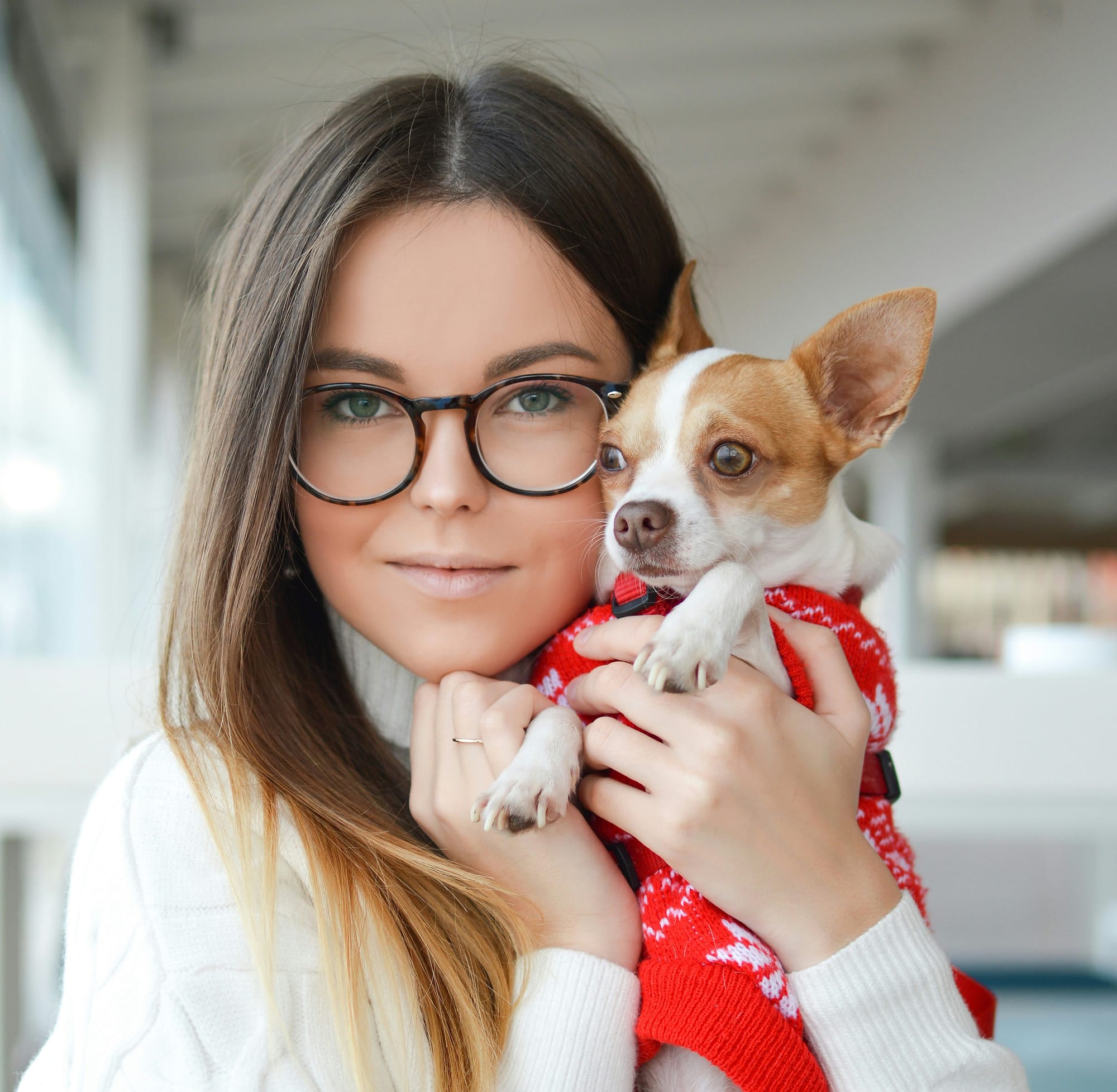 Woman with glasses holding a dog that wears a red sweater